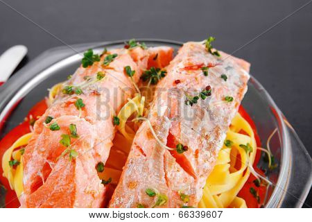 fresh fried natural pink salmon on italian traditional tagliatelle backed with tomato and vegetables served over black wooden table