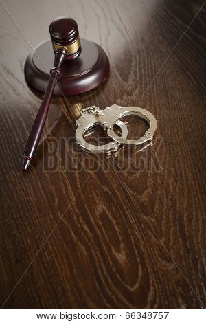 Gavel and Pair of Handcuffs on Wooden Table.
