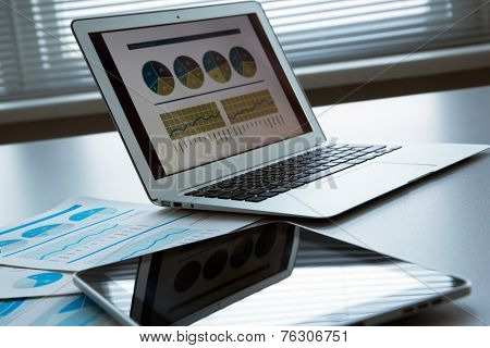 The workplace of business people. Laptop, raphs, charts, business table.