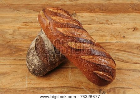 different rye and white flour french bread loaf with on light wooden table background