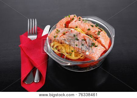 fresh fried natural pink salmon on italian traditional tagliatelle backed with tomato and vegetables served over black wooden table