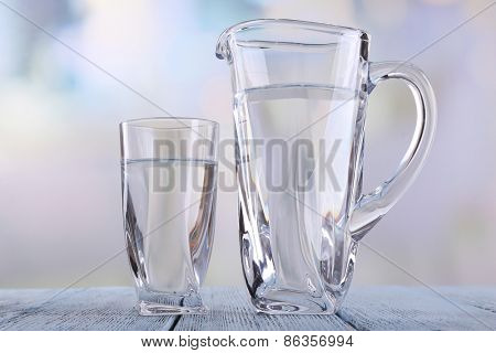 Glass pitcher and glass of water on wooden table on bright background