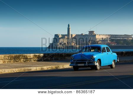 Old Classic Car On Street Of Havana With Ocean And Lighthouse In Background