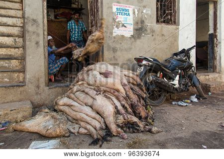 MUMBAI, INDIA - 12 JANUARY 2015: Dharavi slum butcher throws and piles raw sheep skin on street next to parked motorbike.