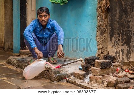 MUMBAI, INDIA - 12 JANUARY 2015: Young Indian man sits and fills water tank in street. Dharavi slum mostly has drinkable tape water in street but not in homes.