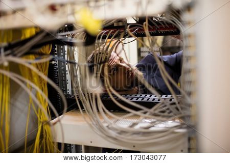 Technician checking cables in a rack mounted server in server room