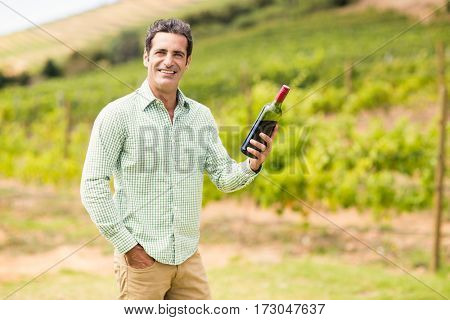 Portrait of smiling vintner holding bottle of wine in vineyard