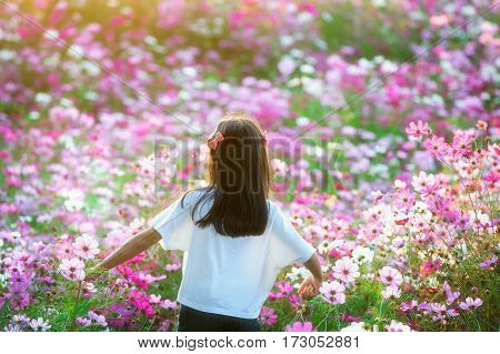 Young girl in a field smelling a pink flower - Cosmos bipinnatus.