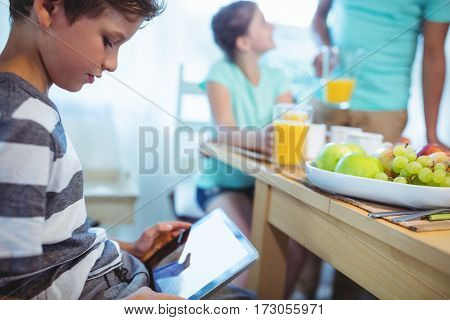 Boy using digital tablet with breakfast on table at home
