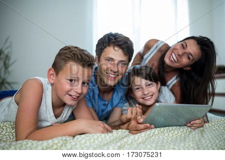 Portrait of happy family using digital tablet in bedroom at home