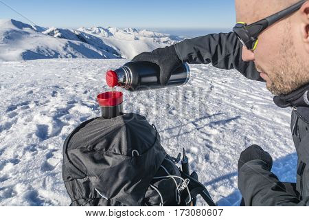 Hiker Pours Hot Tea From A Thermos In The Mountains.
