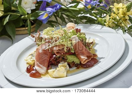 meat salad with ham cheese lettuce Dorblu grapes and olive oil served on a plate on a table with flowers