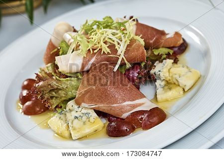 meat salad with ham cheese lettuce Dorblu grapes and olive oil served on a plate on a table with flowers