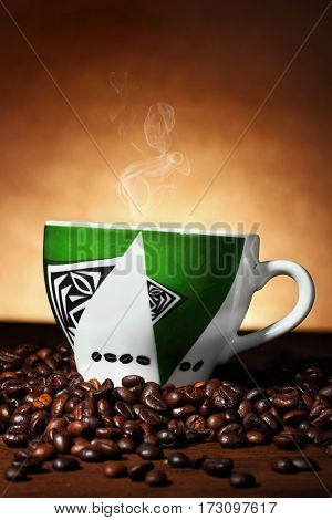 Green cup with african ornament with steaming coffee on coffee beans.Vercal shot