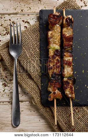 high-angle shot of some barbecued spiced chicken meat skewers on a slate tray, placed on a rustic wooden table