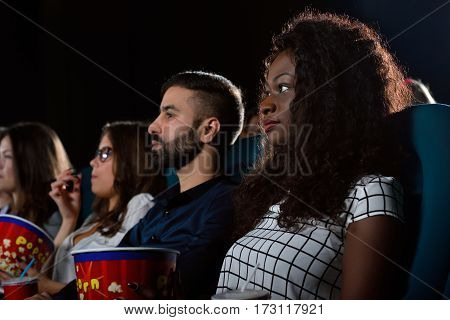 Chilling with friends. Low angle shot of a beautiful African woman watching a movie with her friends at the local movie theatre