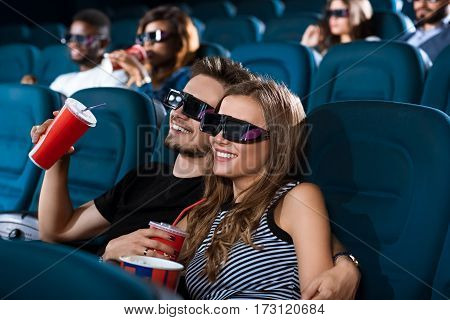 3D love. Gorgeous young couple in love hugging while enjoying a 3D movie at the local movie theatre