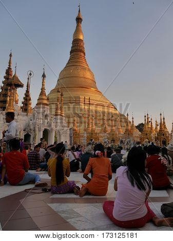 Person kneeing sitting and praying in front of the main stup of Shwedagon Pagoda in city Yangon Myanmar