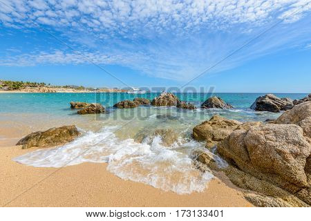 Fantastic sky, ocean and rocks. Differen stages of the waves on the ocean sand. Playa El Chileno Beach, Cabo San Lucas, Mexico.