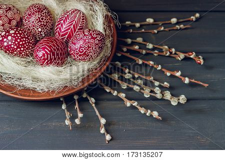 Still life with Pysanka decorated Easter eggs dry willow branches on black wooden background top view copy space