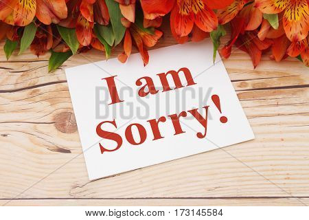 I am sorry message A bouquet of orange lilies on weathered wood with a greeting card with text I am Sorry