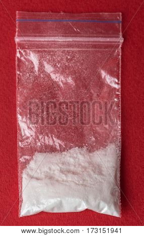 Cocaine in plastic packet on red background, closeup. Portion of drugs. Vertical top view macro photo