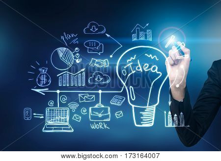 Close up of a hand of a businessman with a blue glowing pen drawing a business sketch and a light bulb on a glassboard. Toned image