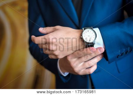 The man in the blue suit looks at his watch, straightens them, hands close up