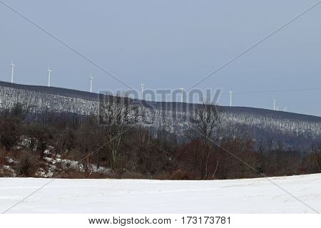Multiple wind turbines working on a snow covered mountain.