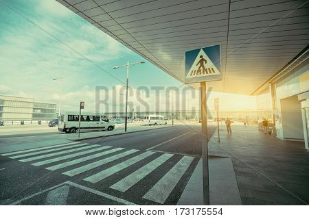 Pedestrian crossing area next to modern contemporary airport terminal entrance zebra traffic cross way with road sing with parking lot and small buses in distance on sunny day in Barcelona Spain