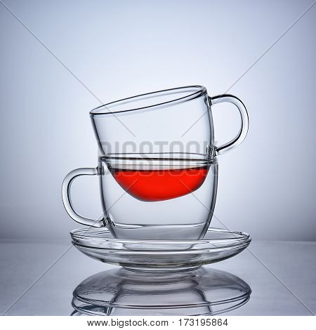 Two cups of clear glass of tea facing each other with saucers.