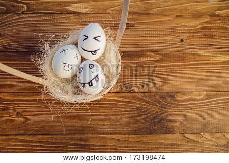 Eggs with painted smiling faces in a basket on wooden bacground