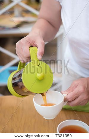female hands close up pouring tea from green coffee in the white cup
