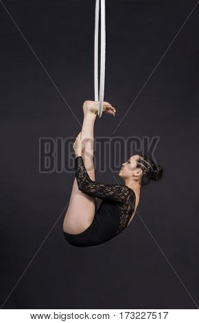 Aerial acrobat in the ring. A young girl performs the acrobatic elements in the air ring. Studio shooting performances on a black background.