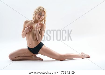 Sporty curly blonde topless sitting in graceful split studio shot