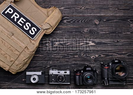 DSLR camera,retro camera and body armor for mass media on dark wooden table.Top view
