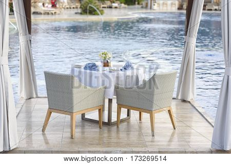 Table with white and blue napkins skateryu for two by the pool. Romantic dinner by the pool.