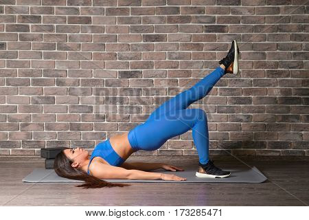 Slim fitness young woman doing plank corp exercise in front of brick wall.