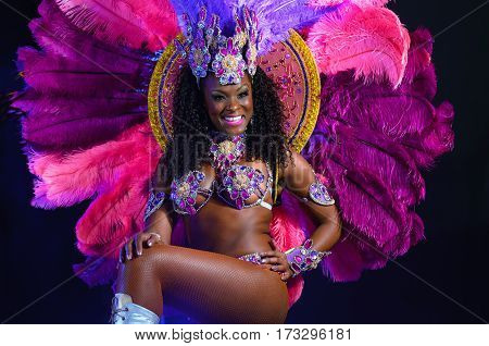 MOSCOW, RUSSIA- JANUARY 2017: Brazilian carnival show. Beautiful girl bright colorful carnival costume dark background. Smiling Afro-Americans woman samba dancer pink carnival costume black background