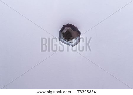 Shrapnel hole on the metal fragment from the white surface