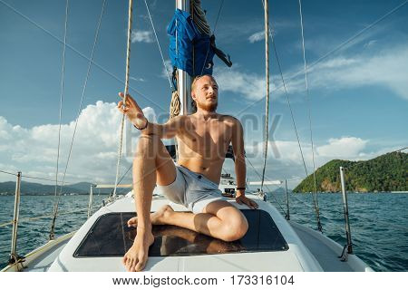 Bearded young man with a mustache sitting on the deck of sailing boat during a walk on the sea. Luxury travel.