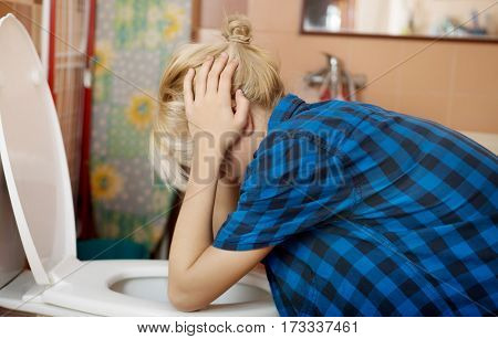 Sick young woman leaning on open toilet seat an vomiting.