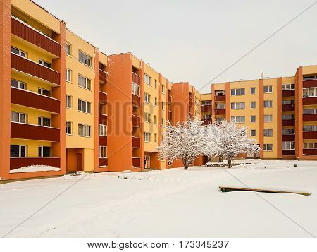 Apartment building yellow-orange, with trees in front covered with snow. Winter city landscape.