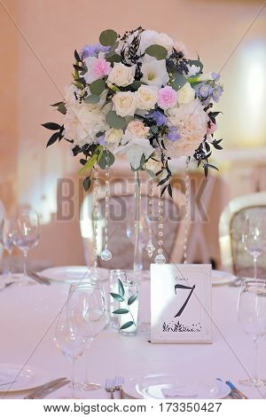 Wedding guest numbered table, decorated with bouquet and settings, in biege and light blue and pink colours