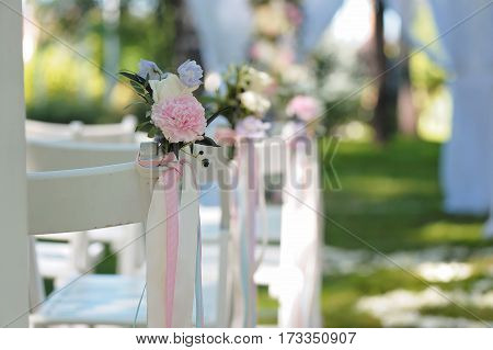 Tenderless boutonnieres on wedding chairs on each side of archway, decorated with biege and blue ribbons, closeup