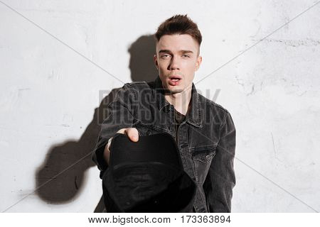 Hipster asks for money in snap back with open mouth and looking at camera over gray background