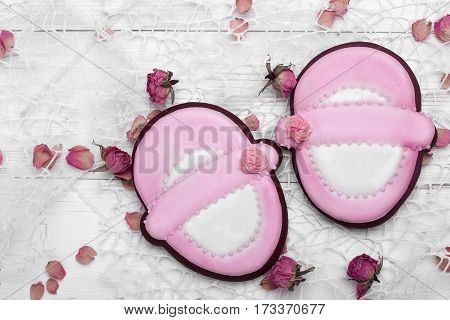 Cookies With Glaze In The Form Of Baby Shoes,with Petals Of Dried Rosses . On White Wooden Surface.