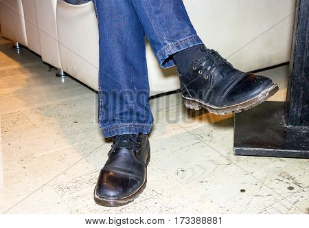 Feet men in jeans and black boots. A man sits on a white sofa