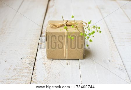 Gift box wrapped in craft paper tied with twine tender small green flower white plank wood background minimalistic copyspace kinfolk