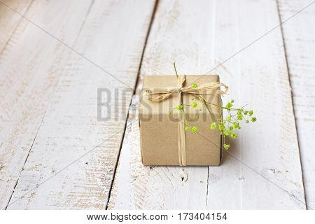 Gift box wrapped in craft paper tied with twine tender small green flower white plank wood background minimalistic copyspace kinfolk top view